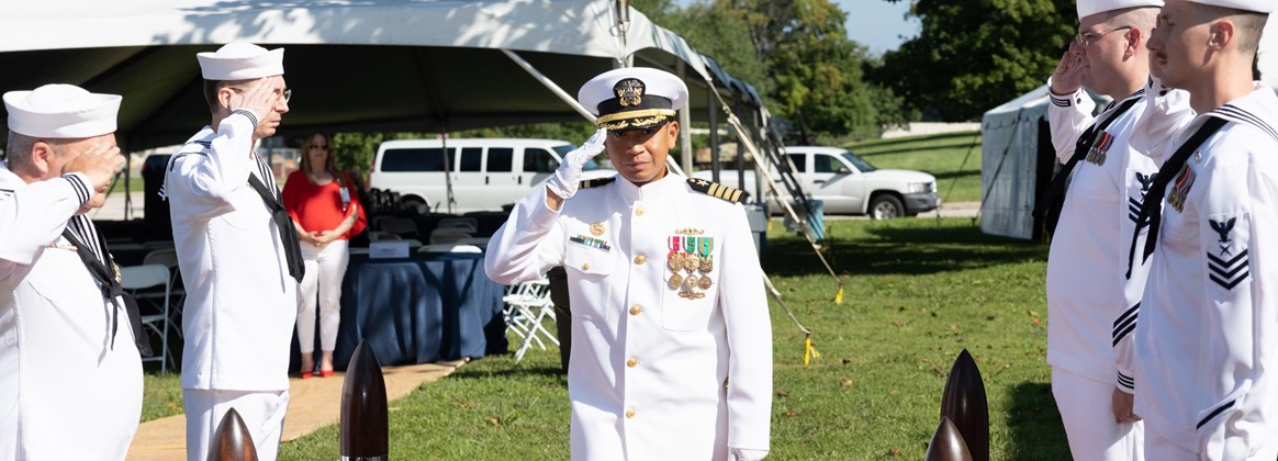 A Navy captain in dress whites salutes other sailors.